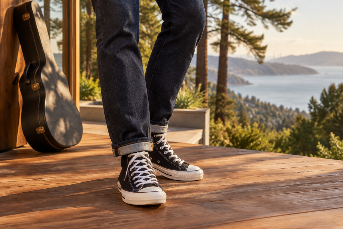 Clean black high-top canvas sneakers and cuffed dark indigo jeans on a sunlit Marin deck, with a guitar case, redwoods and the bay behind