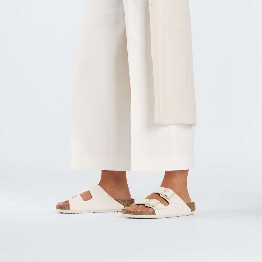 A person wearing off-white double-strap slide sandals with cork-like midsoles, shown from the calves down against a clean white studio background.