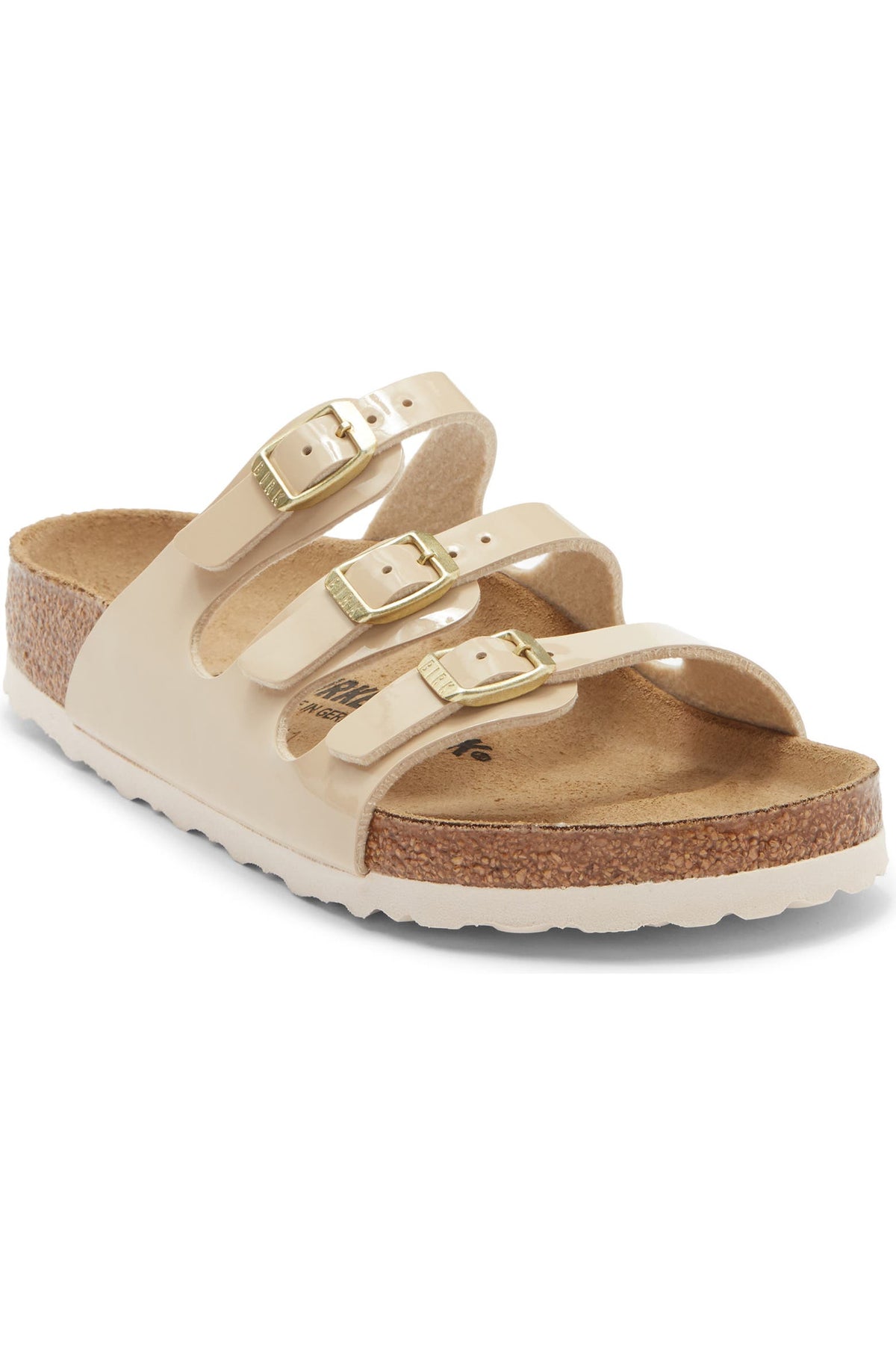 A single double-strap sandal with beige faux-leather straps, gold-tone buckles, a cork midsole, and a white outsole, shown on a plain white background.