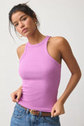 A woman wearing a fitted sleeveless tank top in light purple/lavender with blue jeans and a brown belt, photographed against a plain light gray studio background.