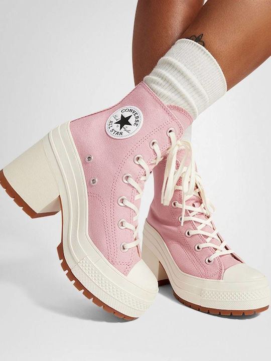 A pair of Converse high-top platform sneakers in light pink canvas with off-white laces, thick cream platform soles, and brown lug outsoles, shown on a model wearing white socks against a light gray studio background.