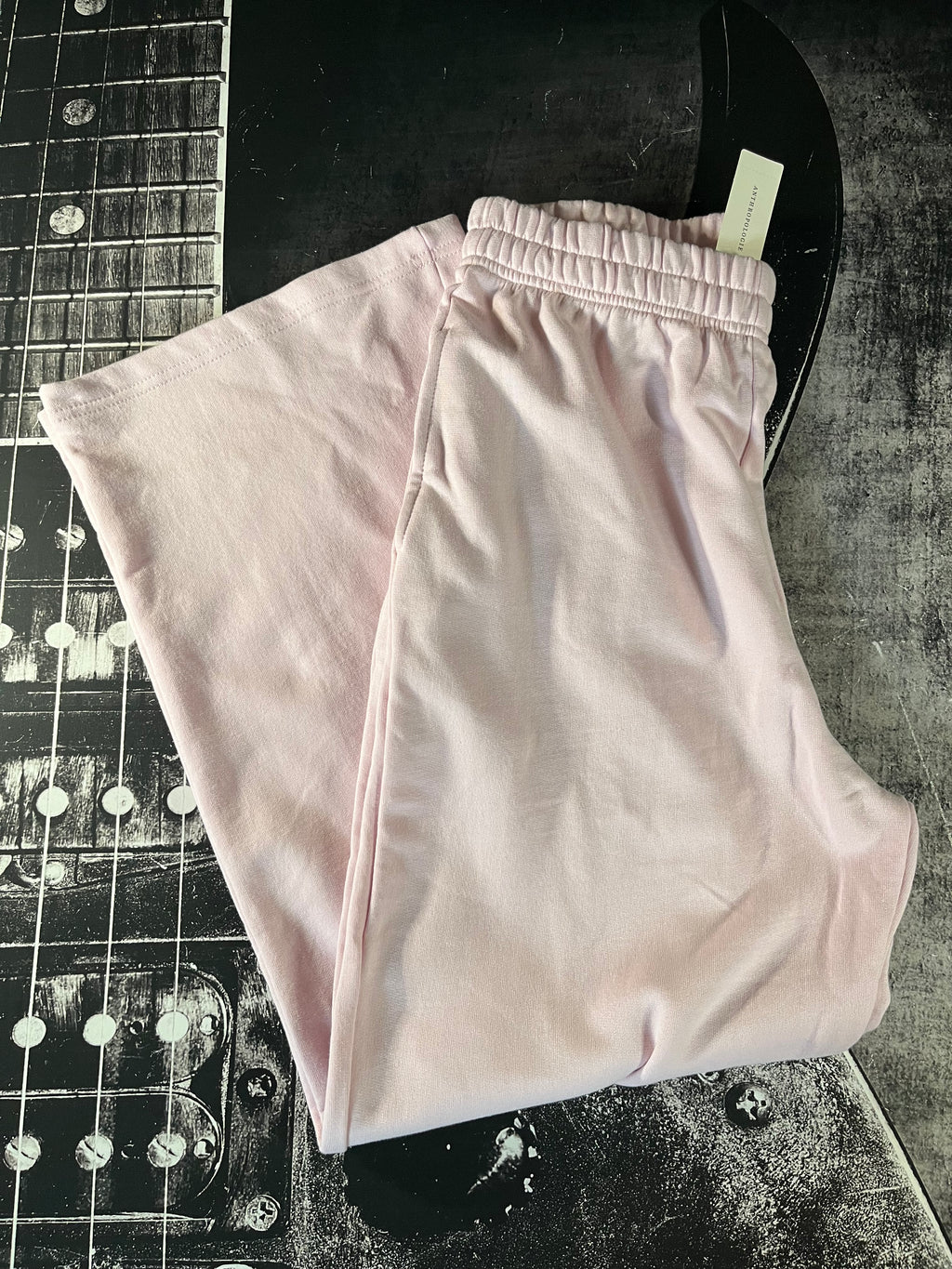 Light pink wide-leg lounge pants folded on a dark textured surface next to a guitar headstock.
