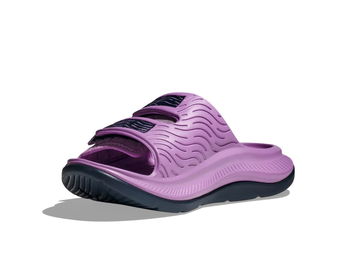 A single women's slide sandal in lavender purple with a wavy textured upper strap and a dark gray sole, shown on a white background with a soft shadow.