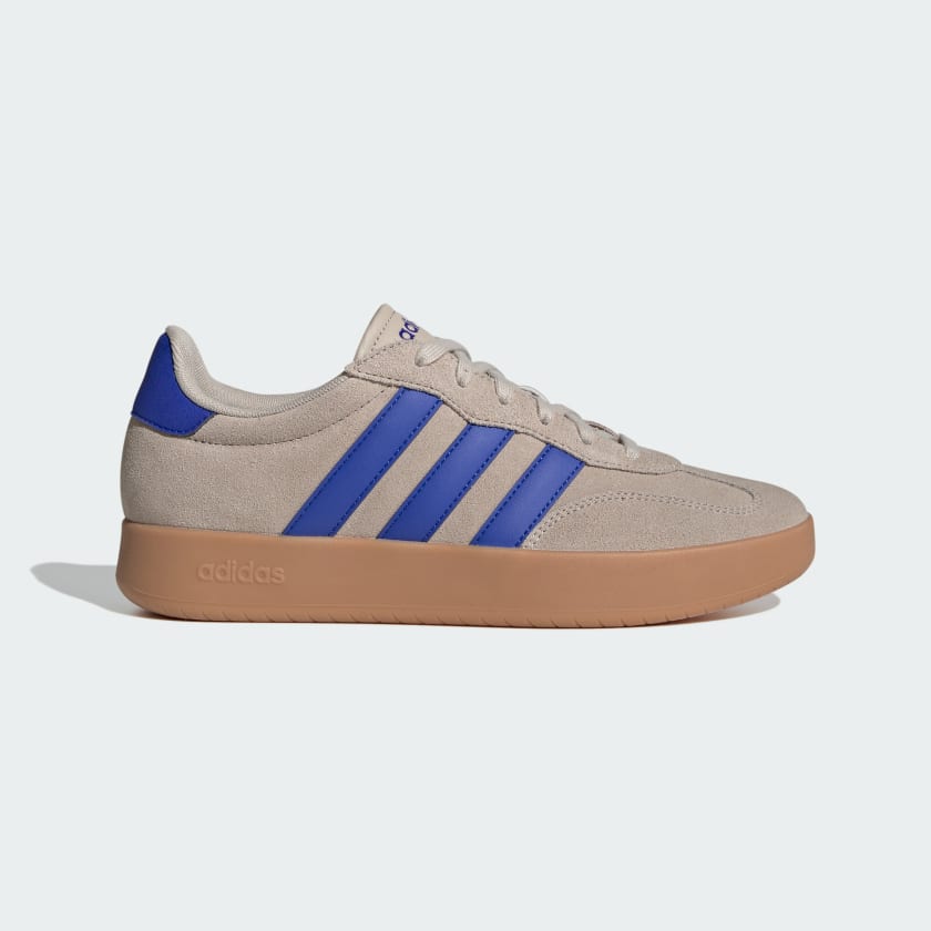 An Adidas low-top sneaker in beige suede with vibrant blue three-stripes, a blue heel tab, and a brown gum sole, shown against a light gray background.