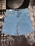Light blue denim shorts with a front split seam, laid flat on a black and white guitar-patterned background.