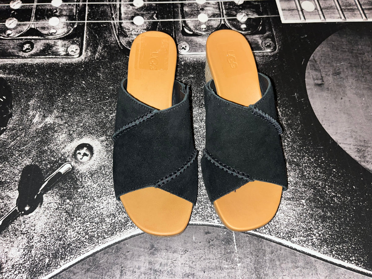 A pair of black open-toe slide sandals with tan soles, photographed from above on a black electric guitar.