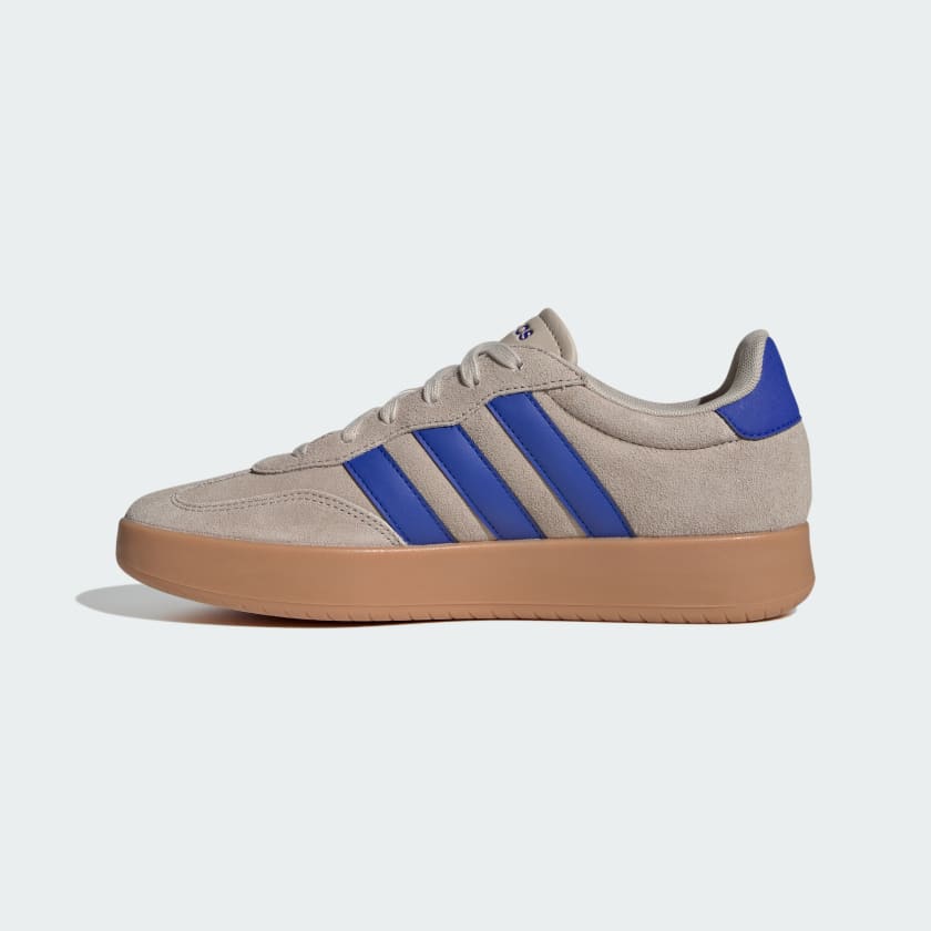 A low-top sneaker in beige suede and canvas with three dark brown stripes, matching brown laces, and a thick brown gum sole, shown in a side profile on a white background.
