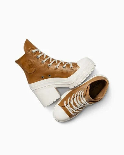 A pair of high-top platform sneakers in tan and white, featuring chunky white platform soles, white laces, and a circular tan logo patch on the ankle.