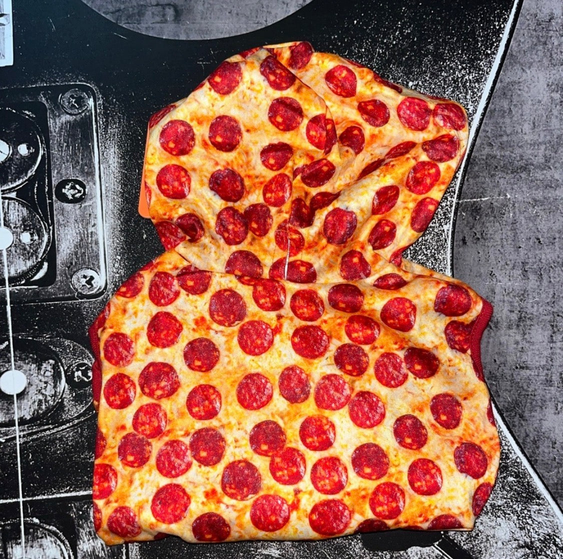 A novelty hooded sweatshirt designed to look like a slice of pepperoni pizza, featuring a printed design of melted cheese, golden crust, and numerous red pepperoni slices, laid flat on a black and gray guitar headstock.