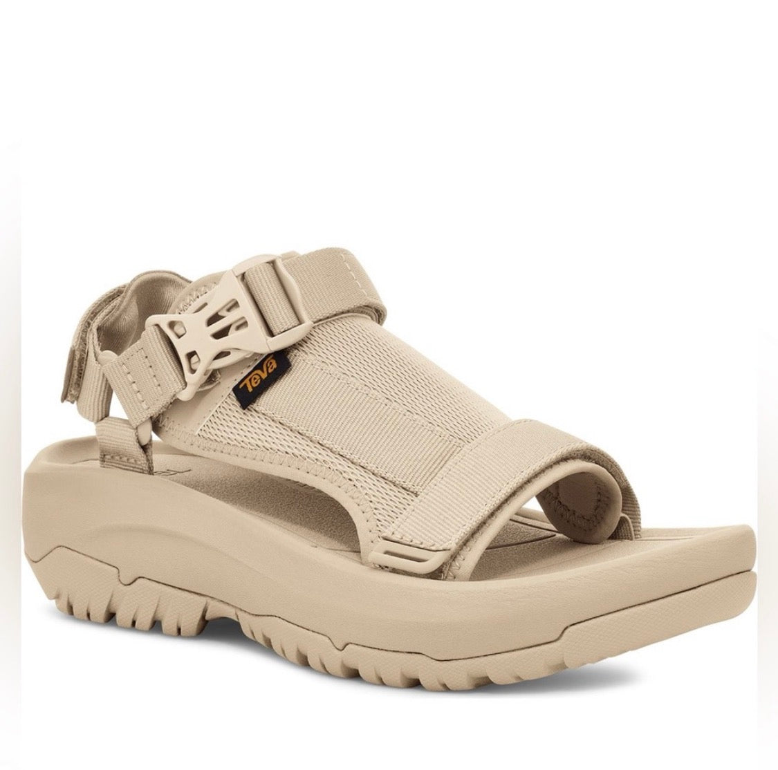A single Teva sandal in a light tan/beige color, featuring a wide adjustable strap with a buckle, a mesh upper band, and a thick, rugged sole, shown against a plain white background.