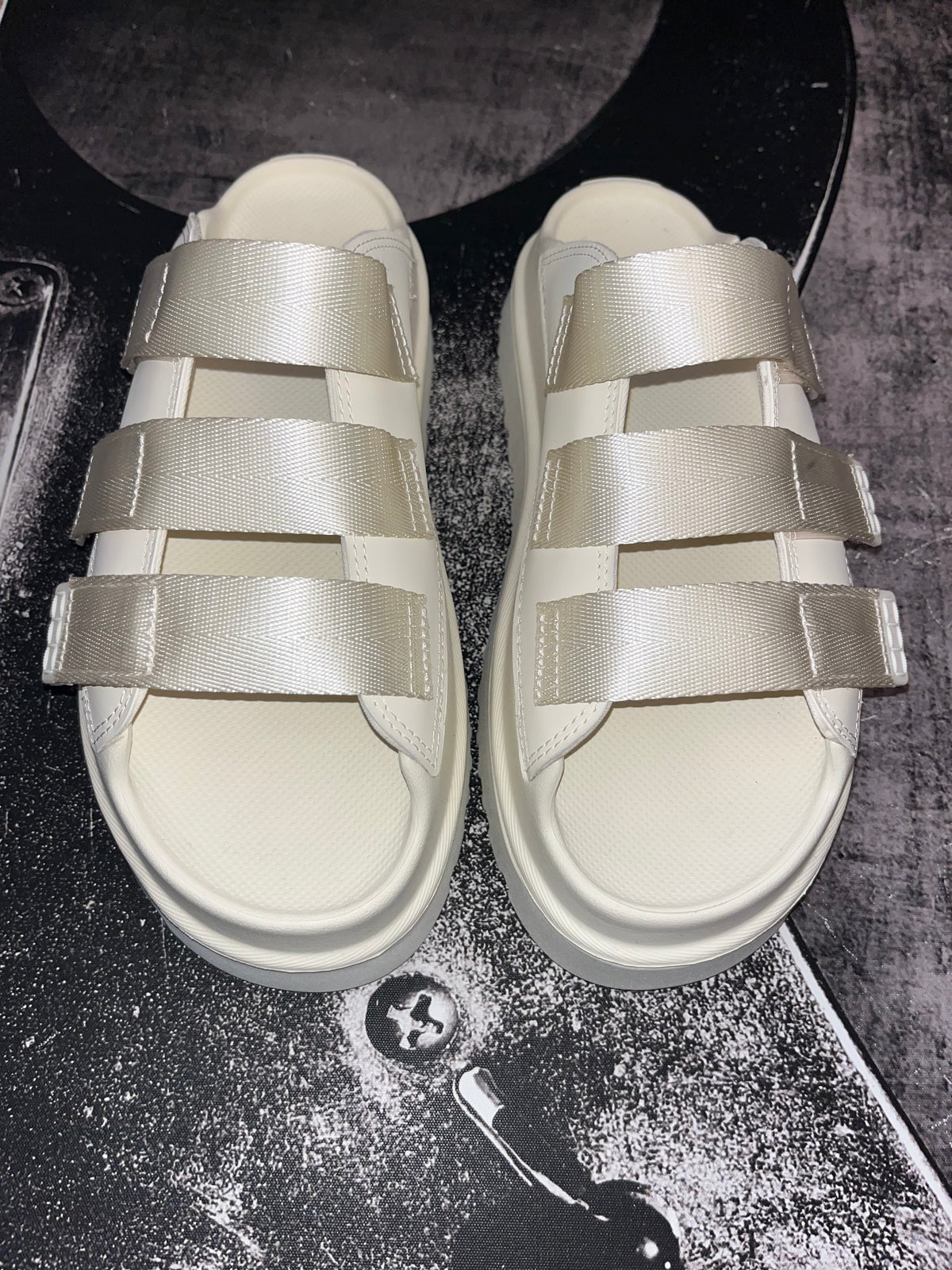 A pair of platform slide sandals with wide, wide-cut satin straps in a champagne beige color, displayed on a dark textured surface.