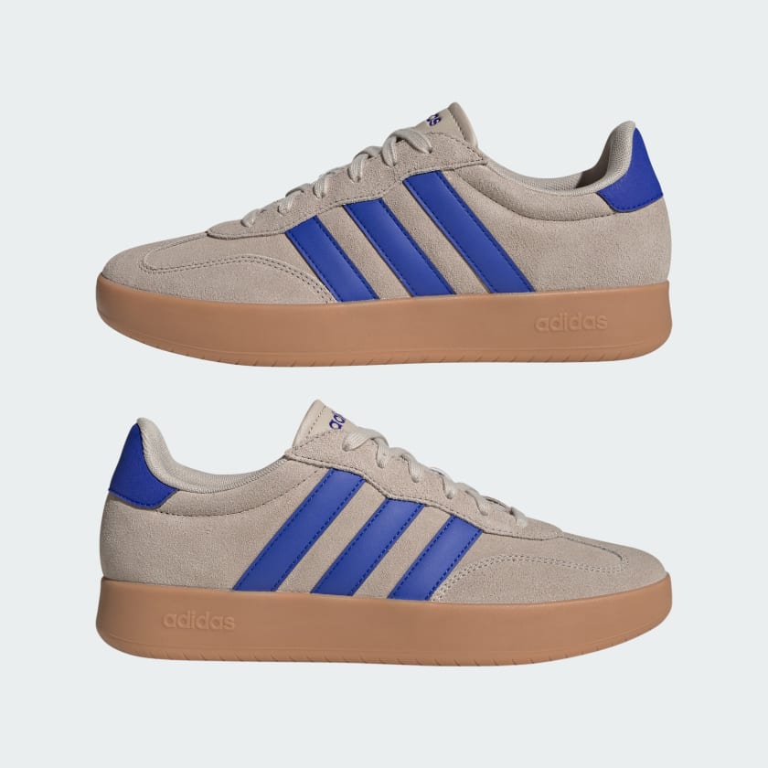 A pair of Adidas low-top sneakers in beige suede with vibrant blue stripes and a gum brown sole, shown from the side on a light gray background.