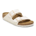 A pair of Birkenstock Arizona double-strap slide sandals in off-white leather with tan buckles and a natural cork footbed, shown on a white background.