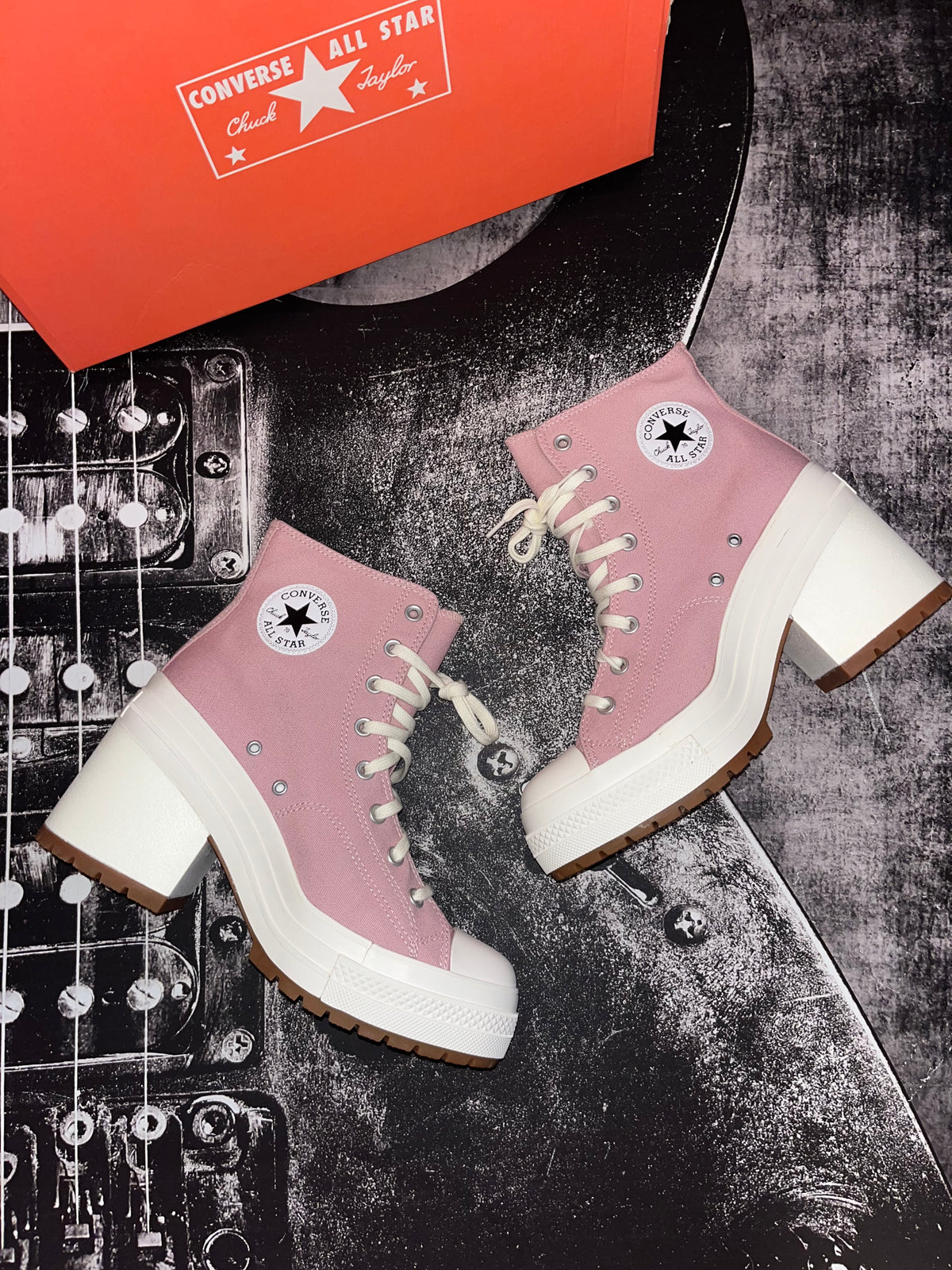 A pair of Converse All Star Cloud ankle boots in dusty pink with chunky white platform soles and white laces, styled on a black electric guitar with an orange Converse box in the background.