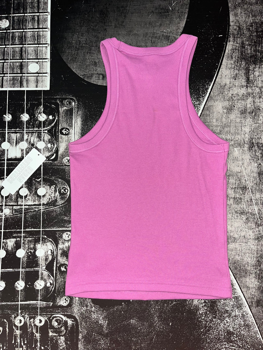 A bright pink sleeveless tank top laid flat on a textured black-and-white guitar body background.
