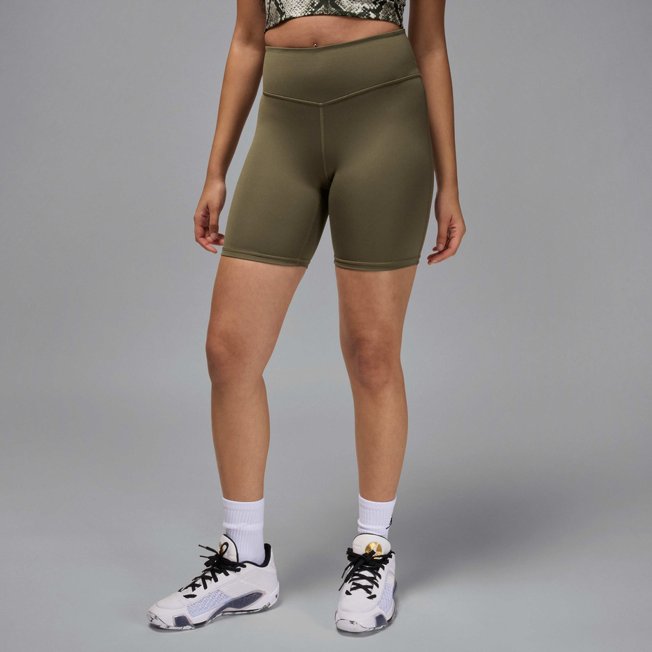 A model wearing olive green high-waisted athletic shorts, white crew socks, and white sneakers with black laces, standing against a solid gray studio background.