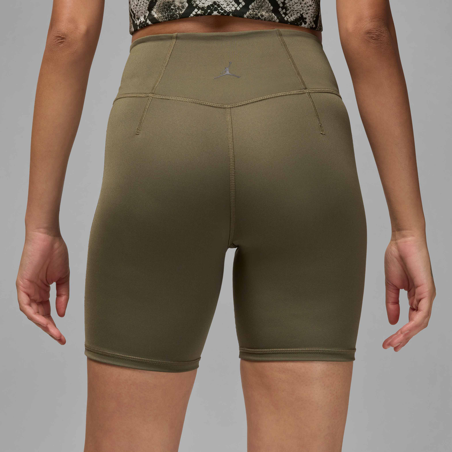 Rear view of a model wearing high-waisted olive green athletic biker shorts with a small gray Jordan logo on the back waistband, set against a solid gray background.